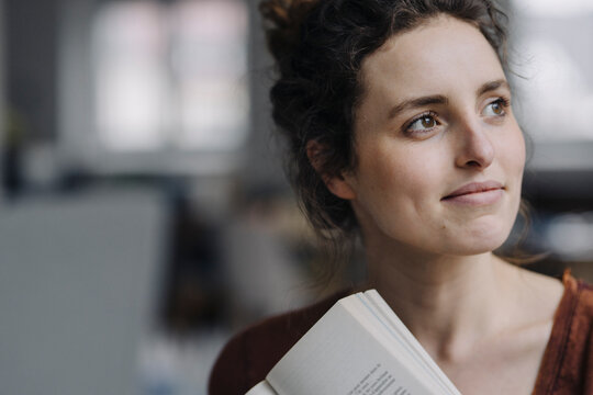 Portrait of smiling young woman with book looking at distance