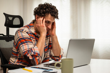 Worried and stressed young businessman using laptop while working from his home.	