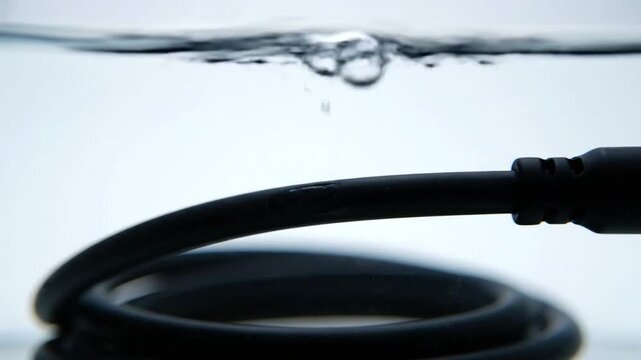 Black electrical cable submerged in clear water with bubbles rising to the surface.