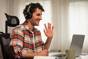 Happy young man talking and waving during video call on laptop while sitting at his comfortable home.	