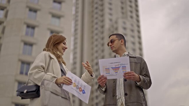 Two dedicated business professionals engage in an impromptu outdoor meeting, meticulously reviewing financial charts and strategizing for future growth, set against a modern urban backdrop.