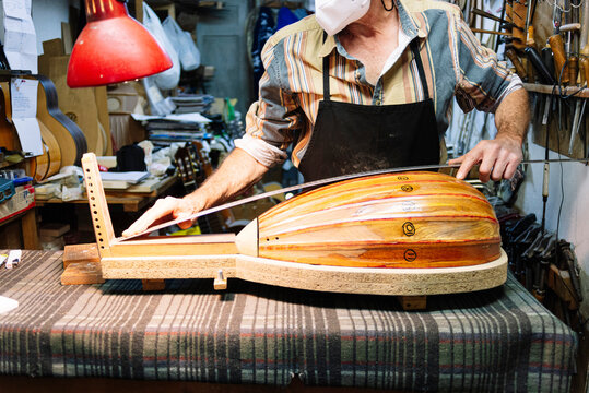 Craftsman with mask measuring lute while standing at workshop