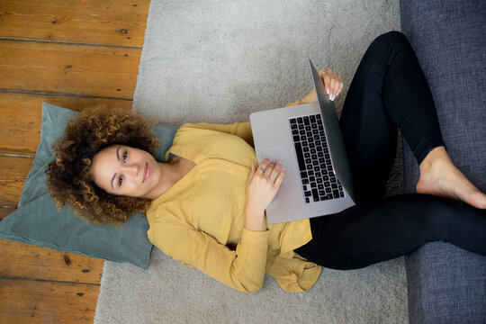 Smiling young woman lying on the floor at home using laptop