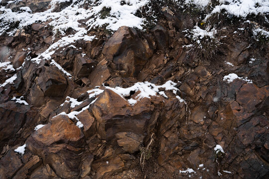 Natural rock texture with grass and snow. Stone background. Winter landscape surface. Outdoor environment. Rugged landscape details.