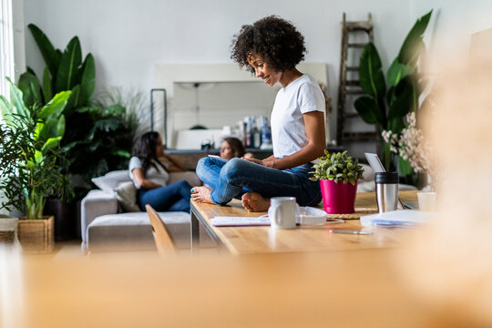 Smiling woman using tablet on table at home with friends in background