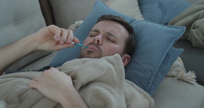 Emotional stock footage showing a sick man lying on a couch with a thermometer, covering his face in frustration, symbolizing illness, financial hardship, lack of healthcare access, and personal crisi