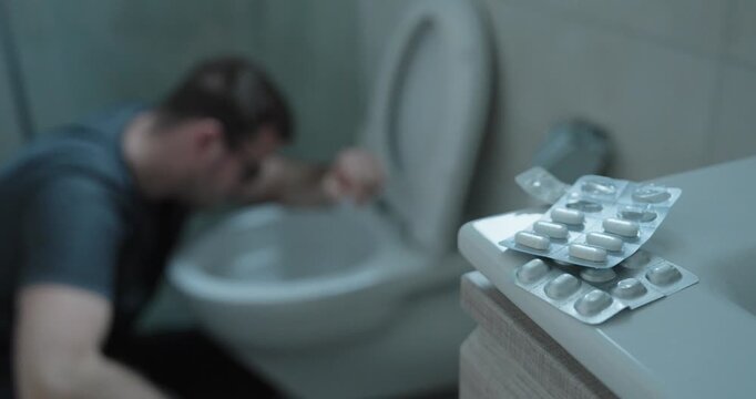 Dramatic stock footage showing a person experiencing nausea near a toilet while medication lies in the foreground, symbolizing side effects, adverse drug reactions, illness