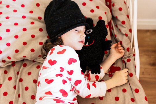 Little girl wearing cap sleeping in bed with her soft toy