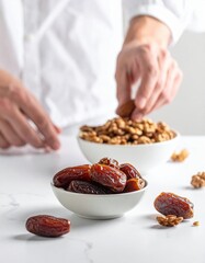 Man in white shirt arranging dates and walnuts in small bowls on a white marble surface with soft natural light casting subtle shadows