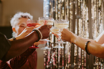 Naklejka premium Diverse group of young adult and middle aged people raising champagne glasses in celebratory toast, hands and arms visible with various skin tones, festive background shimmering