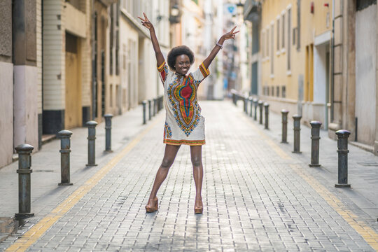 Happy young woman standing with arms outstretched in the middle of a street