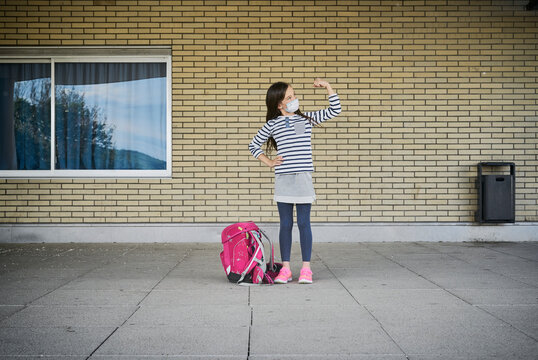 Girl with schoolbag wearing mask standing in front of building flexing her muscles