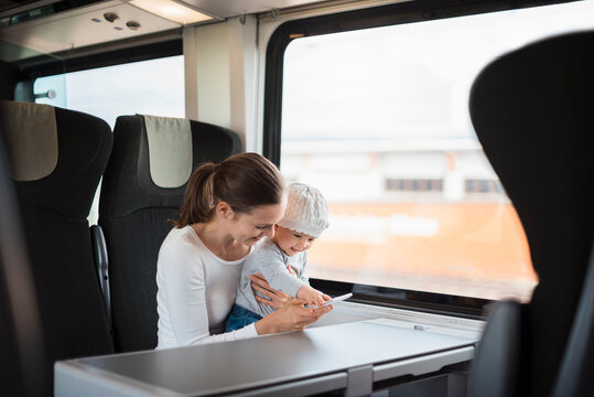 Mother with baby girl traveling by train looking on cell phone