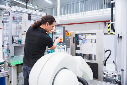 Man operating assembly robot in factory