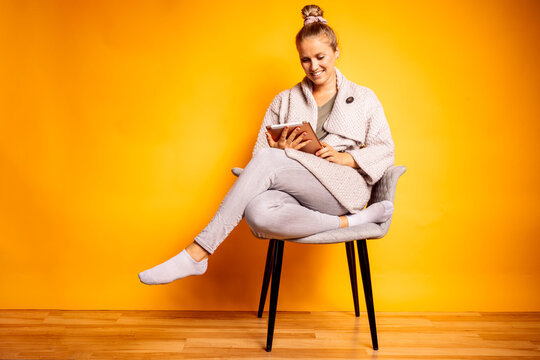 Smiling woman using digital tablet while sitting on chair against yellow background