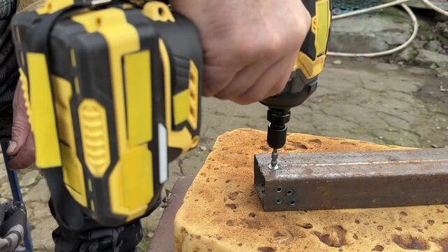cordless drill with Phillips bit tighten screw on rusty metal tube close angle