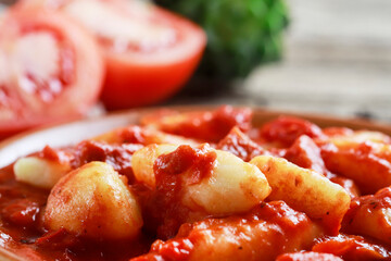 Potato dumplings in a pepper-tomato sauce. Served on a rustic wooden table.