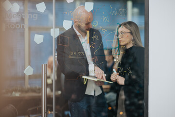 Obraz premium Two business professionals collaborate in a glass meeting room. They brainstorm ideas with drawings and notes on the glass wall.