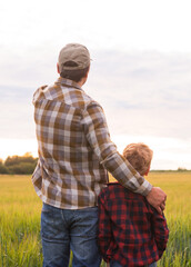 Farmer and his son in front of a sunset agricultural landscape. Man and a boy in a countryside field. Fatherhood, country life, farming and country lifestyle concept.