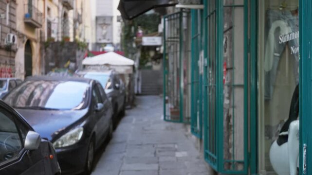Mediterranean narrow street scene with parked cars, teal shop grills and stone pavement, defocused shallow street; background backplate copyspace calm.