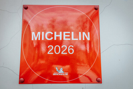 Red Michelin plaque displaying the year 2026, featuring white text and a logo, mounted on a textured wall with visible cracks and imperfections