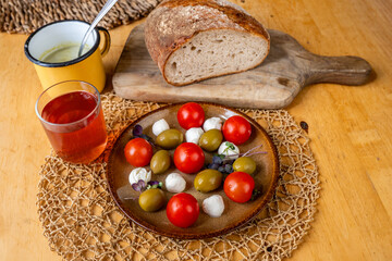 Plate with mini mozarella, cherry tomato and olive, glass of fruit tea and bread.