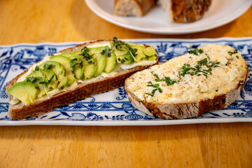 Two sliced bread on plate, first is with avocado, second is with egg spread.