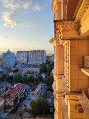 Cityscape with sea and blue sky on summer evening and sunlight illuminated white wall with windows of multi-story residential building. Old buildings, roofs, green trees. Front facade. Architecture