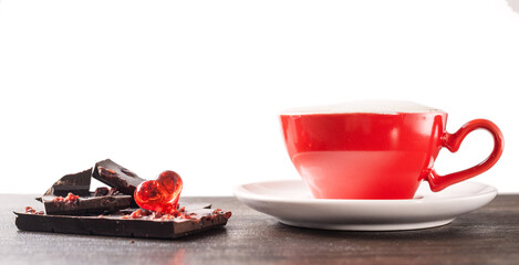 A cup of delicious, aromatic coffee with chocolate pieces and a red heart on a dark background