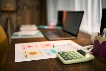 Closeup showing desk with financial charts, calculator, laptop and stationery arranged for lesson preparation, emphasizing workspace setup for tutor or student learning session