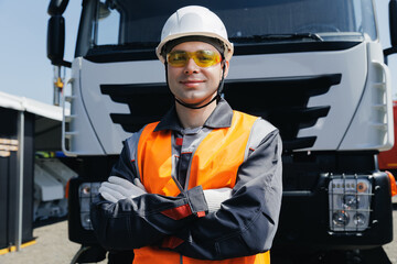 Happy Young male driver of construction vehicle, worker standing confidently in front of truck