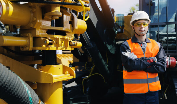 Confident male construction worker in safety gear standing by heavy rig drilling machinery outdoors