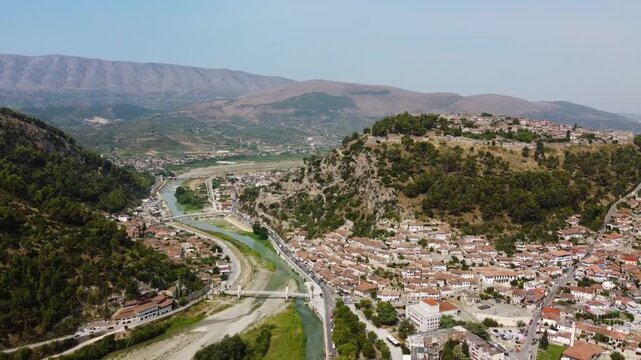 Wide aerial drone footage of Berat, Albania, showing the historical architecture of the Mangalem and Gorica districts on a sunny summer day.