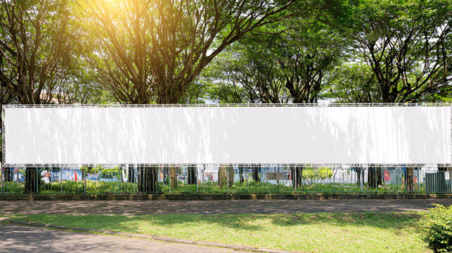 Long white vinyl banner on fence in urban park, Blank hoarding mockup, billboard, signage in city with green blossoming spring trees. Commercial advertisement, public information canvas. Mock up space