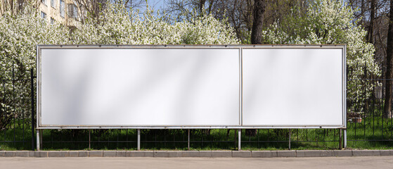 Long white vinyl banner on fence in urban park, Blank hoarding mockup, billboard, signage in city with green blossoming spring trees. Commercial advertisement, public information canvas. Mock up space