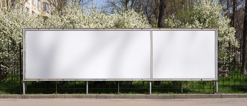 Long white vinyl banner on fence in urban park, Blank hoarding mockup, billboard, signage in city with green blossoming spring trees. Commercial advertisement, public information canvas. Mock up space