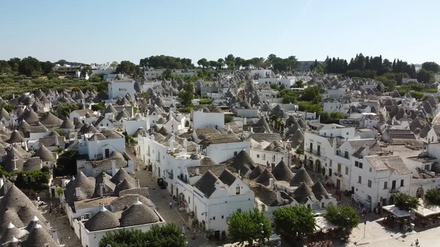Aerial drone footage of Alberobello, Italy on a bright sunny day. The iconic trulli houses with their cone-shaped stone roofs are captured from above, showcasing the historic UNESCO World Heritage tow