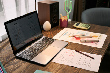 Open laptop displaying lesson graphs sitting on wooden desk with printed test paper marked with C...