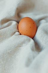 Orange egg resting on soft fabric with folds in a close-up setting during daylight hours