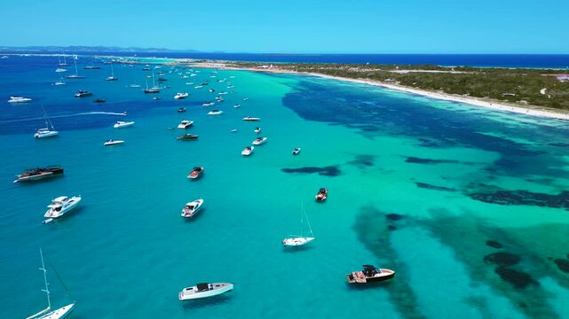 Formentera coastline, boats in tranquil turquoise sea. Smooth aerial view drone
