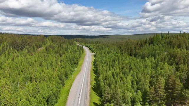 Aerial, forward drone flight, forest in Swedish Lapland. A straight asphals road is deviding the forest in 2 parts. At the end, the road makes a turn. Wonderful green pine trees. No cars visible.