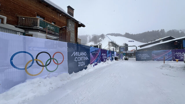 Livigno, Italy - February 4, 2026: Snowy access road and temporary fencing with Milano Cortina 2026 Winter Olympics branding at the Livigno freestyle and snowboard venue during heavy snowfall