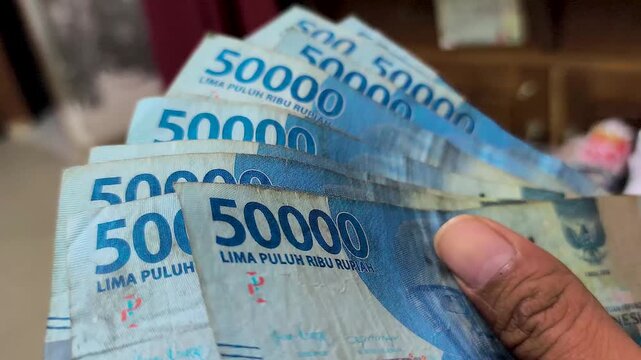 An adult's fingers holding an Indonesian fifty thousand rupiah banknote