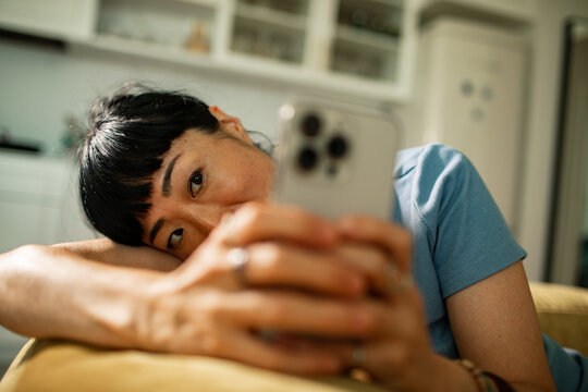 Tired woman lying on couch using smartphone at home