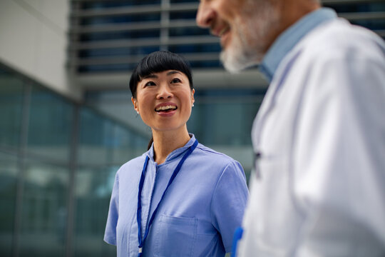 Smiling nurse talking with senior doctor outside hospital