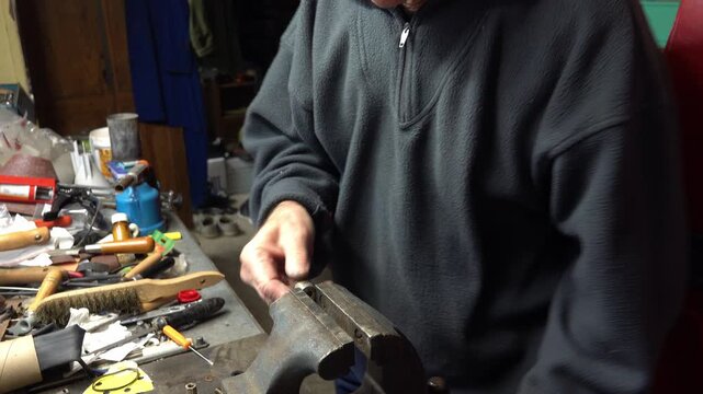 A person handles tools at a workbench in a garage