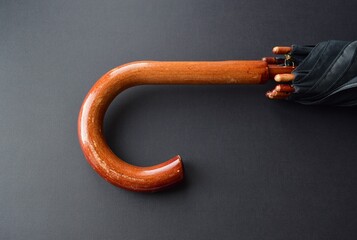 Wooden handle of a black folding umbrella on a black background