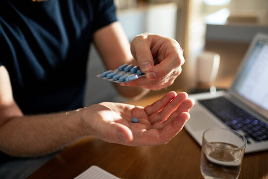 Man taking blue pill at home workspace