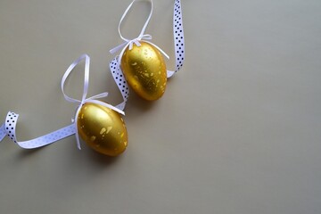 Two golden chicken eggs with ribbons on a dark background. Minimalistic Easter background