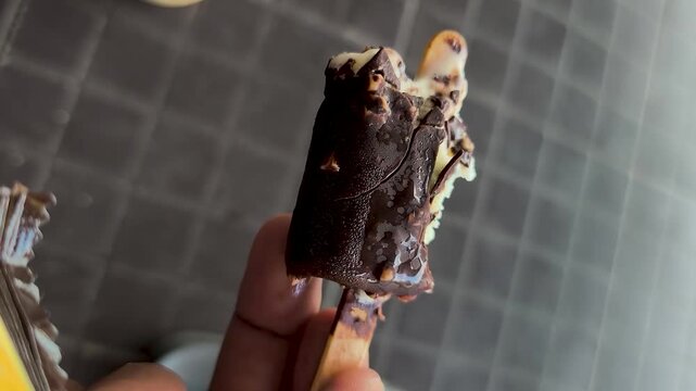 A hand holding a chocolate ice cream, with bite marks visible and a delicious taste.